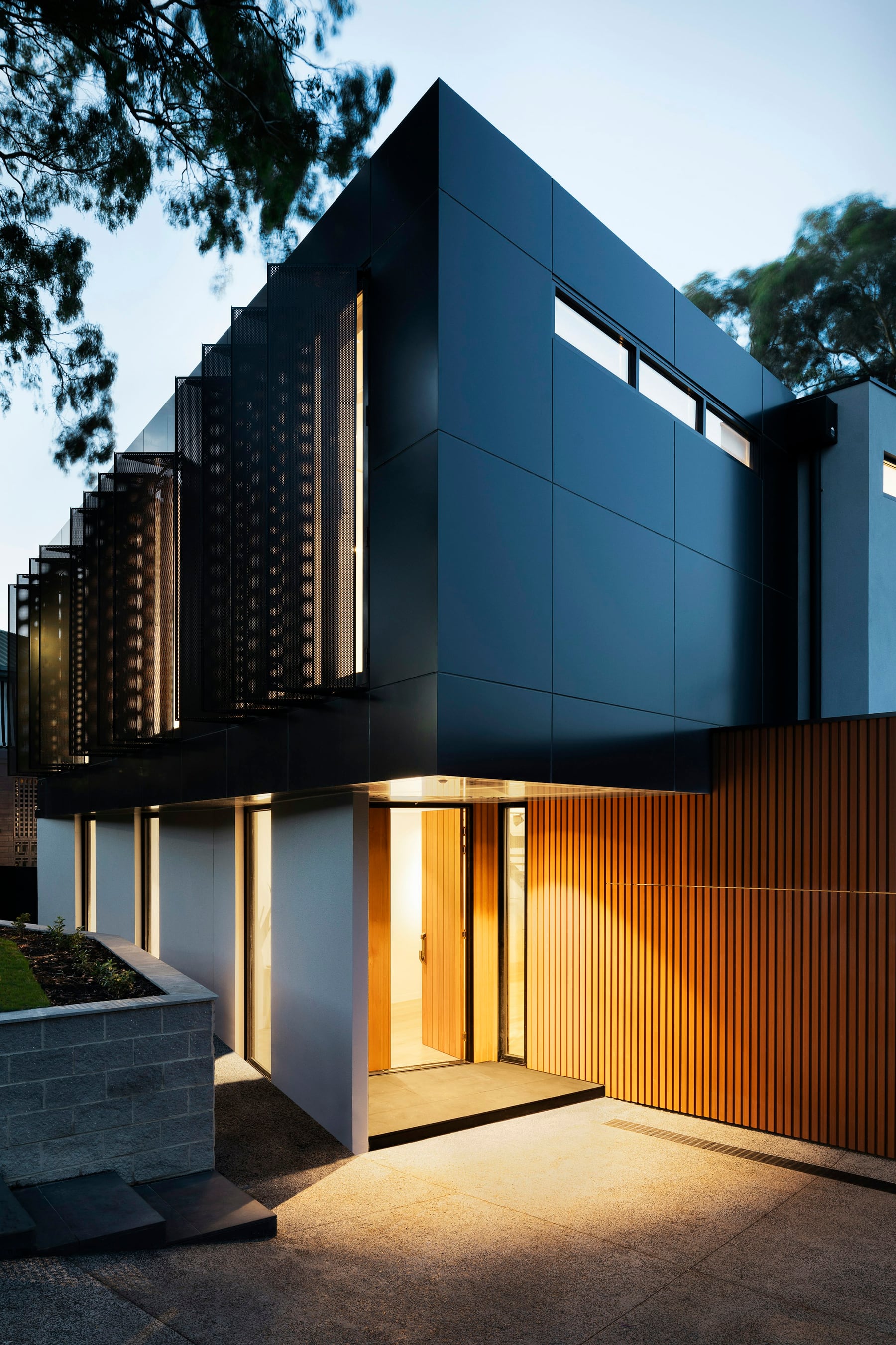 Modern custom home with charcoal architecture, warm wood cladding, and a glowing entry at dusk