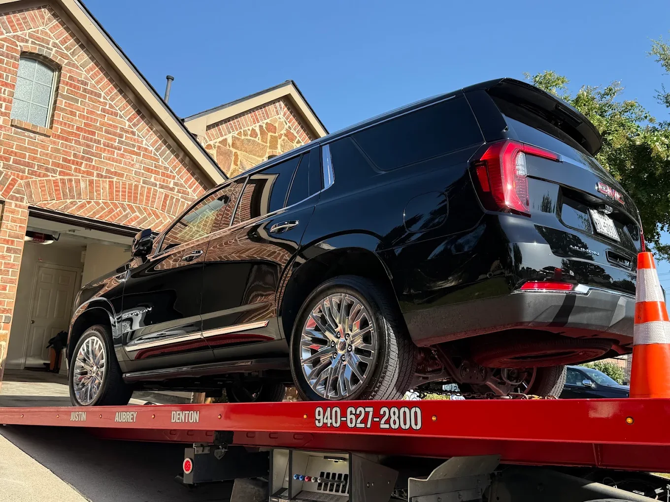 All American flatbed loading a GMC Yukon in a residential driveway